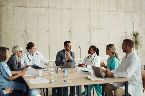 Réunion de travail avec des médecins et un homme au centre en costume portant des lunettes autour d'une grande table